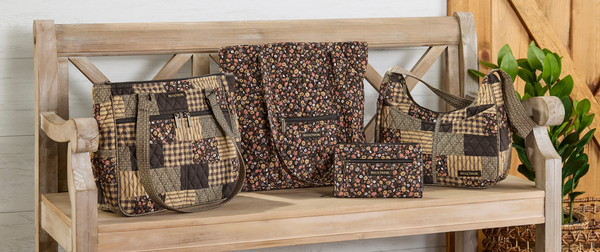 A coordinated set of patchwork and floral fabric tote bags and a small matching pouch arranged on a wooden bench, with a potted plant and rustic wall in the background.